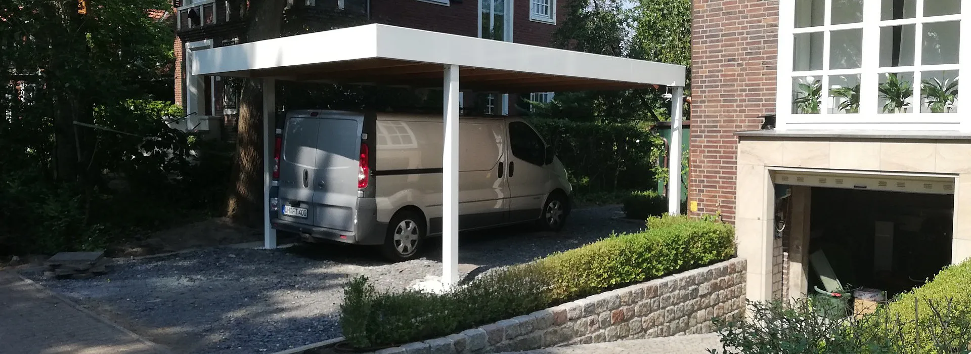 anthrazit farbenes Carport aus Metall, mit Holzdach in Einfahrt mit angrenzendem Zaun