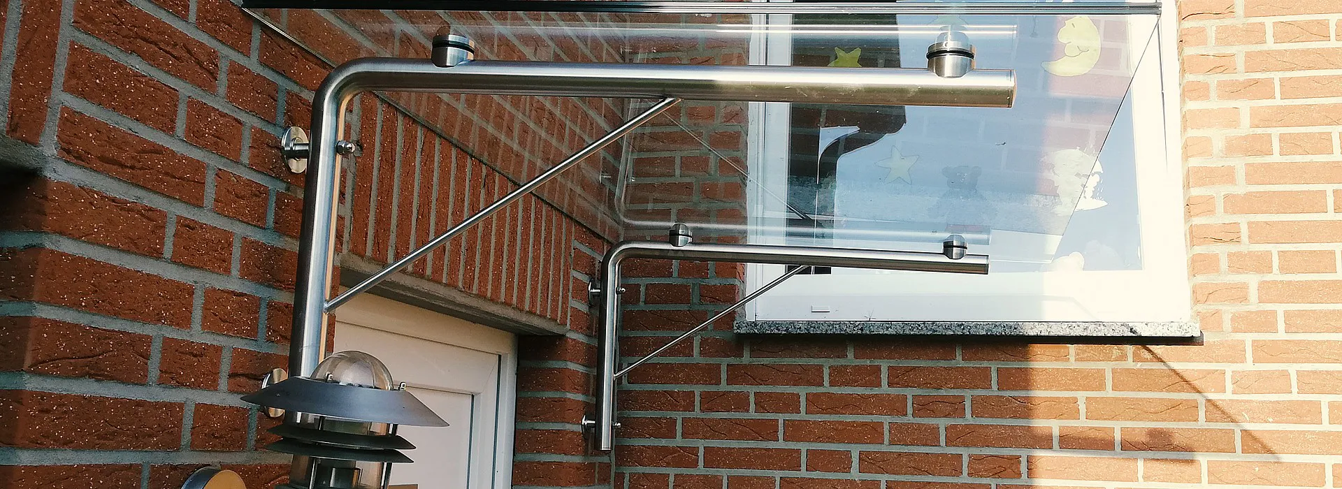Glasvordach über Haustür mit rechtwinkliger Metallhalterung an Wand