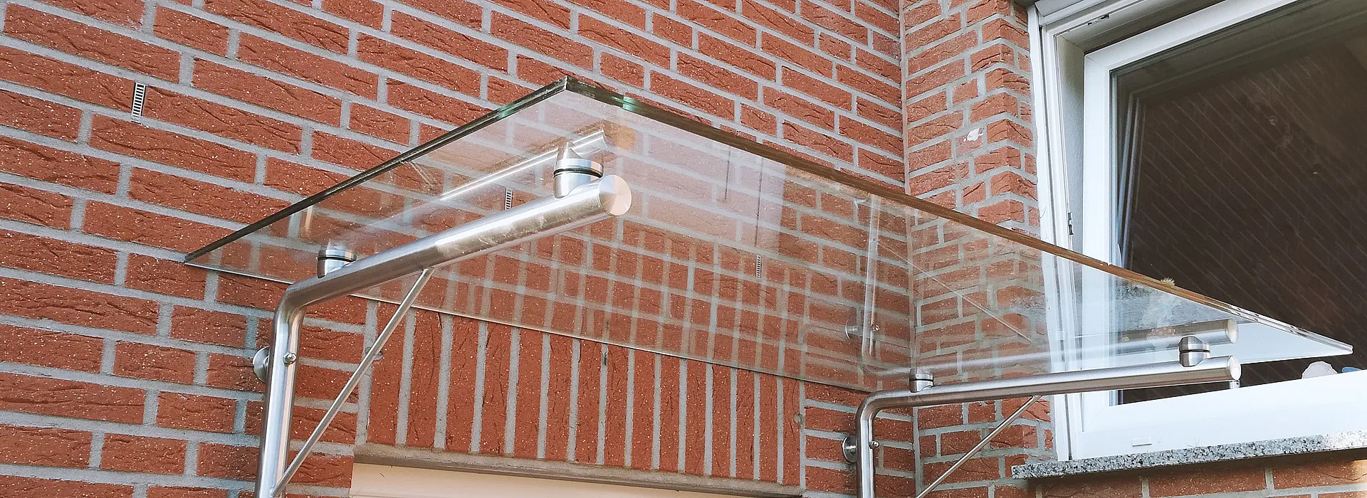 Glasvordach über Haustür mit rechtwinkliger Metallhalterung an Wand, Seitenansicht