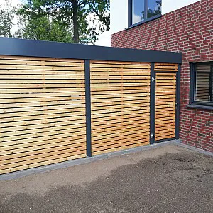 Anthrazit farbenes Carport aus Metall und Holz in Einfahrt mit angrenzendem Holzschuppen, Seiteneingang